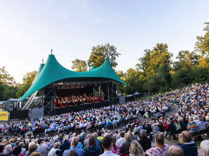 Tausende Gäste schauen auf die Bühne. Auf der Bühne spielt ein Orchester.
