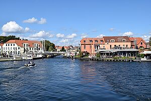 Im Vordergrund: die Müritz. Dahinter schieben sich Häuser der Malchower Innenstadt ins Bild. Eine Brücke verbindet an einem Kanal beide Uferseiten.