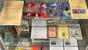 Eine Vitrine. Darin liegen Bücher und Info-Texte. Die Bücher enthalten Sagen.