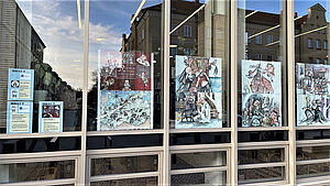 Große Fenster. In den Fenstern hängen bunte Illustrationen.