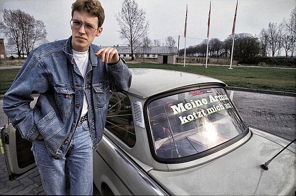 Das Foto zeigt einen Mann. Er lehnt an einem Auto. Auf der Autoscheibe steht: Meine Armut kotzt mich an.