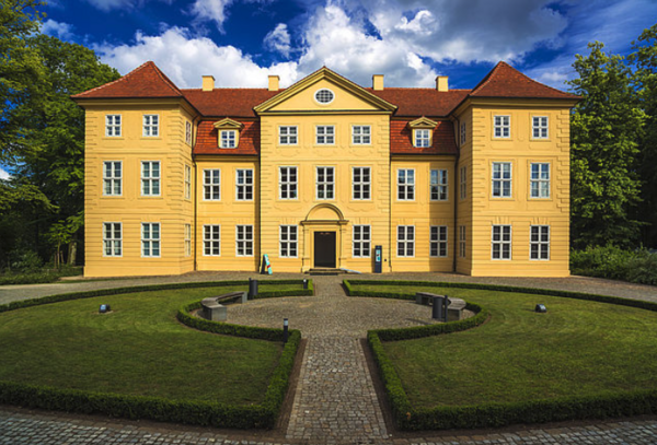 Das Schloss Mirow. Zwei Halbkreise aus Wiese liegen einander zugewandt. Dazwischen verläuft ein Weg Richtung Eingang.