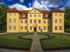 Das Schloss Mirow. Zwei Halbkreise aus Wiese liegen einander zugewandt. Dazwischen verläuft ein Weg Richtung Eingang.