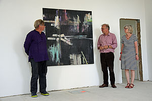 Ein Mann und eine Frau der Kunstkommission stehen vor einem großflächigen Gemälde von Wolfram Sulek. Der Künstler steht daneben.