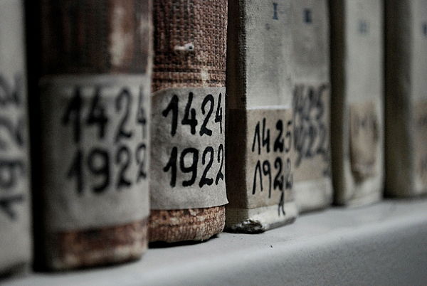 Ein Ausschnitt von einem Regal, in dem historische Bücher nebeneinander stehen. Der Fokus liegt auf Etiketten mit Jahreszahlen, die am Buchrücken angebracht sind. 