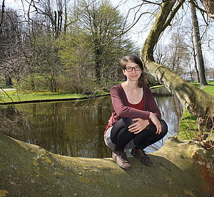 Sarah Fischer hockt auf einem umgefallenen Baumstamm an einem See.