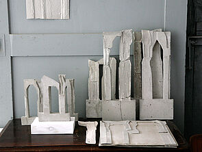 An der Wand lehnen Teile von Skulpturen.