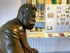 Eine Bronzeskulptur von Reuter. Dahinter, an der Wand, befindet sich eine Glasvitrine mit Infos, Fotos und Büchern.