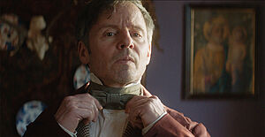 Ein Mann. Er prüft im Spiegel den Sitz seiner Fliege.