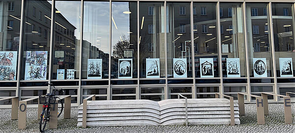 Ein Gebäude mit schmalen, hohen Fensterscheiben. In den Scheiben hängen Scherenschnitte mit Märchenfiguren.