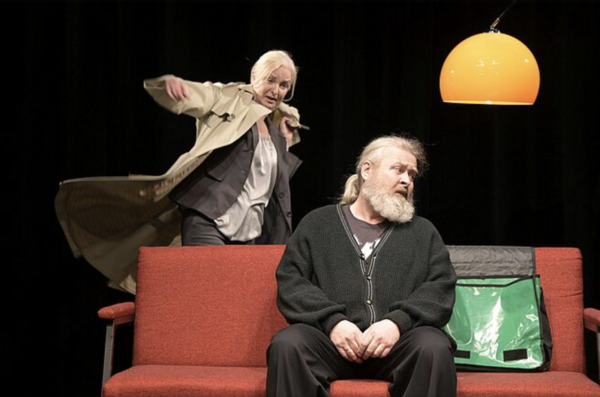 Zwei Schauspieler auf der Bühne. Der Mann sitzt. Die Frau wirbelt hinter ihm.