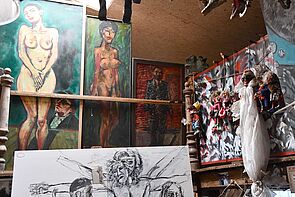 Das Atelier von Hans W. Scheibner ist groß. Es hängen sehr viele Gemälde im Raum. Auch Marionetten hängen von der Decke.