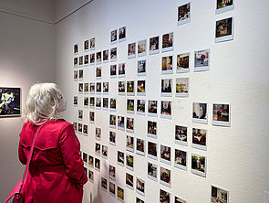 Eine Besucherin betrachtet eine Wand voller Polaroids.