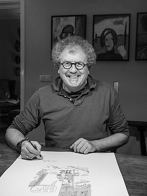 Ein Mann sitzt an einem Tisch und zeichnet eine Karikatur.