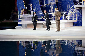 Drei Schauspieler stehen auf der Bühne und sprechen.