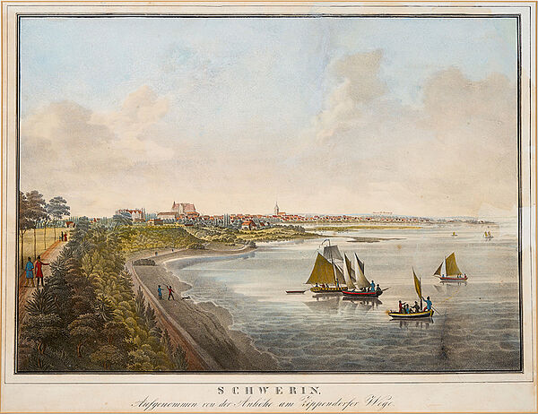 Ein See. Auf dem See sind Segelboote. Am Ufer wachsen Bäume und Pflanzen. Auf einem Weg gehen Menschen. Im Hintergrund stehen viele Häuser.