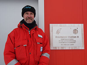 Horst Bornemann steht neben einem Schild mit der Aufschrift "Neumayer-Station III".