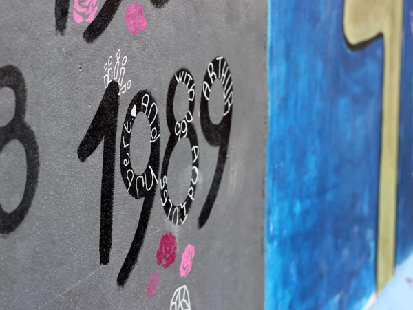 An einer grauen Mauer stehen Zahlen. Eine davon: 1989.