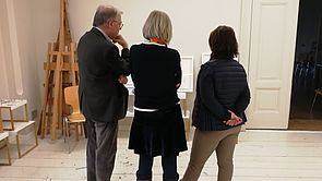 Drei Mitglieder der Kunstkommission stehen vor Bildern der Künstlerin.
