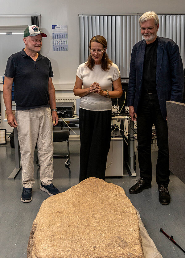 Peter Wittenberg, Kulturministerin Bettina Martin und Landesarchäologe Dr. Detlef Jantzen stehen nebeneinander vor dem Bildstein. 