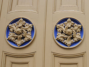 Die Tür an der Westfassade trägt auf jedem Flügel ein sandfarbenes Ornament, das in einen blauen Kreis eingelassen ist. 