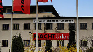 An einer Gebäudefassade hängt die Aufschrift "Dokumentationszentrum Prora". Weiter unten hängt ein Schild mit der Aufschrift "MACHTUrlaub". 
