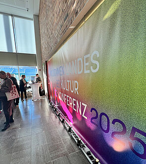 Ein Plakat hängt in einem Saal. Eine Ankündigung für die Landeskulturkonferenz.