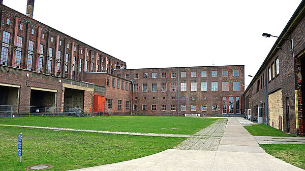 Der Hof des Museums ist an drei Seiten von mehrstöckigen Backsteingebäuden umgeben. Im Hof wächst Wiese und führt ein Weg entlang.  