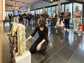 Eine Frau kniet vor einer Kunst-Installation. Menschen schauen zu.