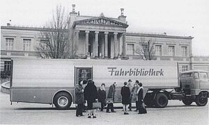 Ein langer LKW. Auf dem Anhänger steht "Fahrbibliothek". Vor der geöffneten Tür im Anhänger stehen Leute. Eine Schwarz-Weiß-Aufnahme.