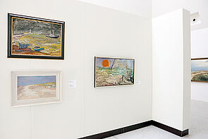 Blick in einen Ausstellungsraum. Vorn hängen Bilder an der Wand.