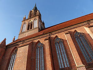 Die Perspektive zeigt vier große gotische Fenster des Backsteinbaus und wandert den Kirchturm hinauf in den blauen Himmel.