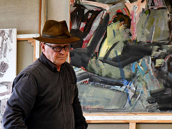 Ein Mann vor einer Malerei. Daneben Skizzen.