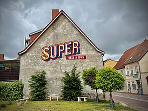 Eine Hauswand. Auf der Wand steht dieses Wort geschrieben: Super.