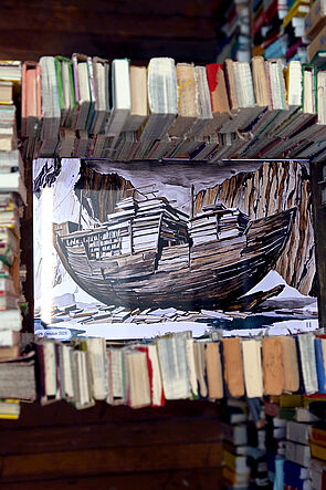 Auf Büchern liegt ein Gemälde. Es zeigt ein Schiff aus Holz.
