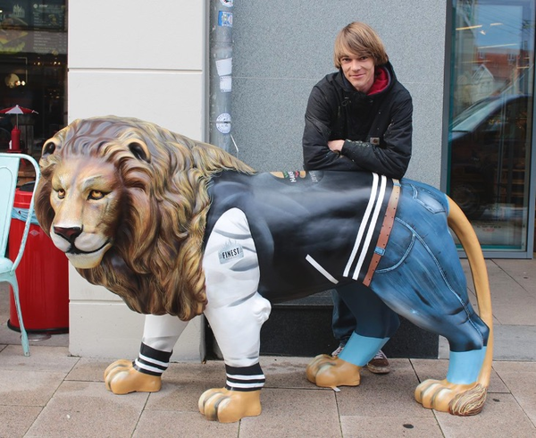 Daniel Wrede steht draußen, hinter einem Modell-Löwen und stützt sich auf dessen Rücken.