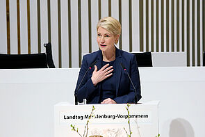 Eine Frau steht an einem Pult und spricht ins Mikrofon.