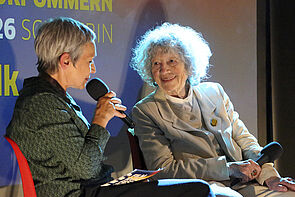 Filmgespräch auf der Bühne. Mit einer Moderatorin und einer Frau.