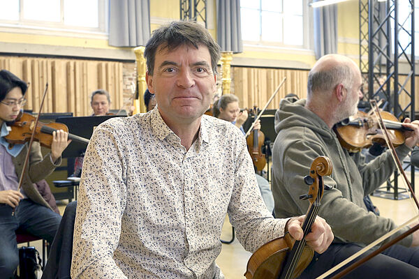 Volker Reinhold mit einer Geige. Hinter ihm andere Musiker mit Instrumenten.