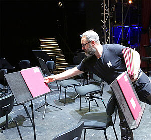 Ein Mann legt eine farbige Mappe auf ein Orchesterpult.