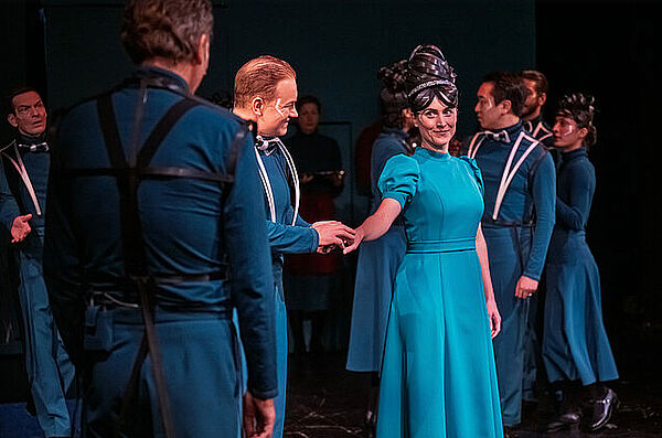 Auf einer Bühne stehen mehrere Leute. Eine Frau reicht einem Mann die Hand. Nur die Frau ist von vorn zu sehen.