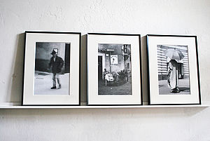 Auf einem Regal an der Wand lehnen drei Schwarz-Weiß-Bilder in schwarzen Rahmen.