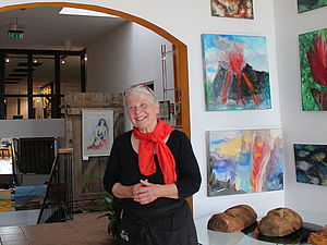 Karola Glaser steht in einem Raum im Kunsthaus. Hinter ihr an den Wänden hängen gemalte Bilder.