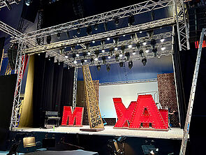 Eine Bühne. Auf der Bühne stehen Requisiten. Zum Beispiel große rote Buchstaben.