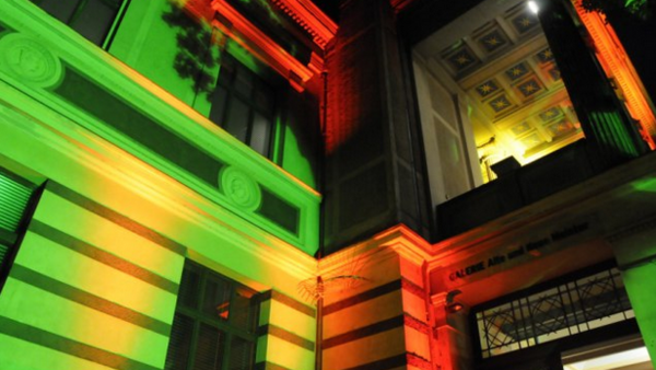 Ein dicht aufgenommener Ausschnitt der Fassade vom Staatlichen Museum. Sie wird angestrahlt in den Farben grün, gelb und rot.