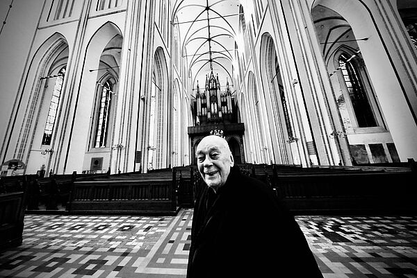 Ein Mann steht in einer Kirche. Im Hintergrund scheint Licht durch die Fenster.
