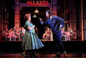 Ein Mann spricht gestikulierend mit einer Frau. Die Frau weicht vor ihm zurück. Beide tragen Kostüme.