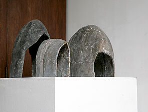 Drei graue Büsten auf einem weißen Sockel.