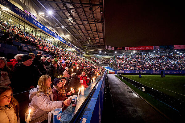 Tausende Menschen im Stadion. Sie halten Kerzen in den Händen und singen.
