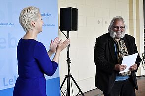Ministerpräsidentin Manuela Schwesig applaudiert Wolfgang Bordel zu. Er steht neben ihr mit einer Urkunde in der Hand.